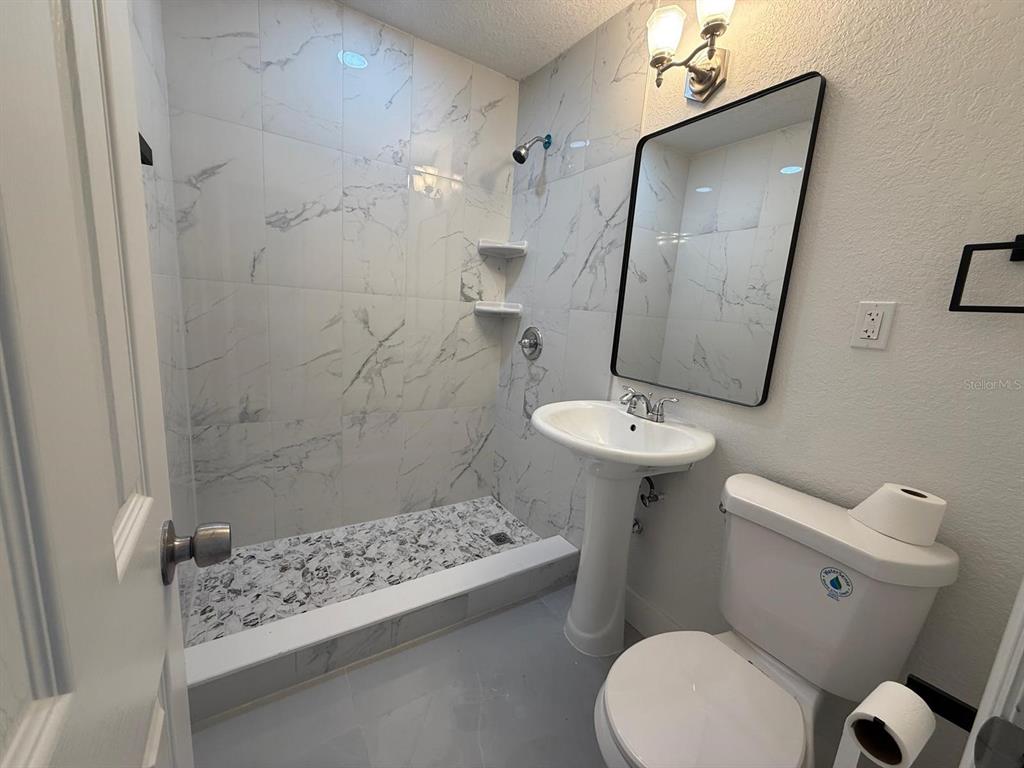 A bathroom features a walk-in shower with marble-look tile, a pedestal sink, and a toilet — 427 40TH AVENUE S, ST PETERSBURG, FL