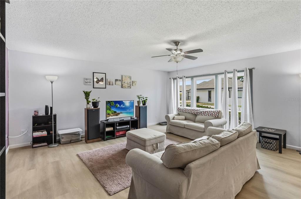A living room features light wood flooring, a beige sofa, a television, and a ceiling fan — 1489 MAGELLAN CIRCLE UNIT 603, ORLANDO, FL