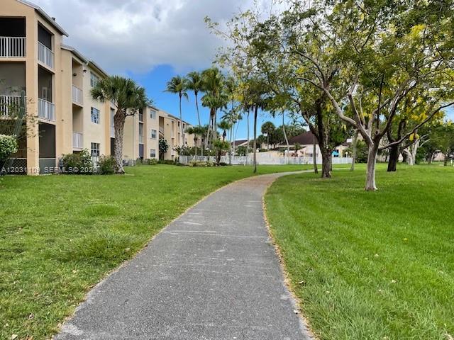 A paved walkway winds through a grassy lawn beside a multi-story apartment building — 15275 SW 107th Ln # 102, Miami FL 33196, MIAMI, FL