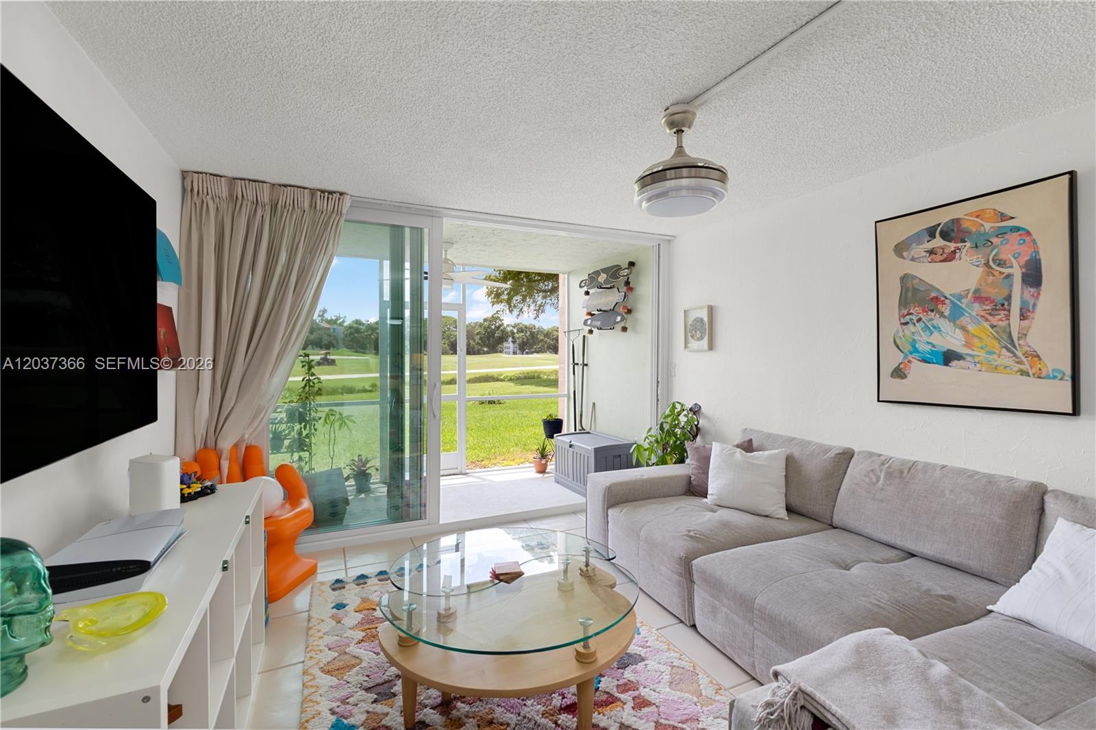 A living room features a gray sectional sofa, glass coffee table, and sliding doors to a patio — 9495 Evergreen Pl # 103, Davie FL 33324, DAVIE, FL
