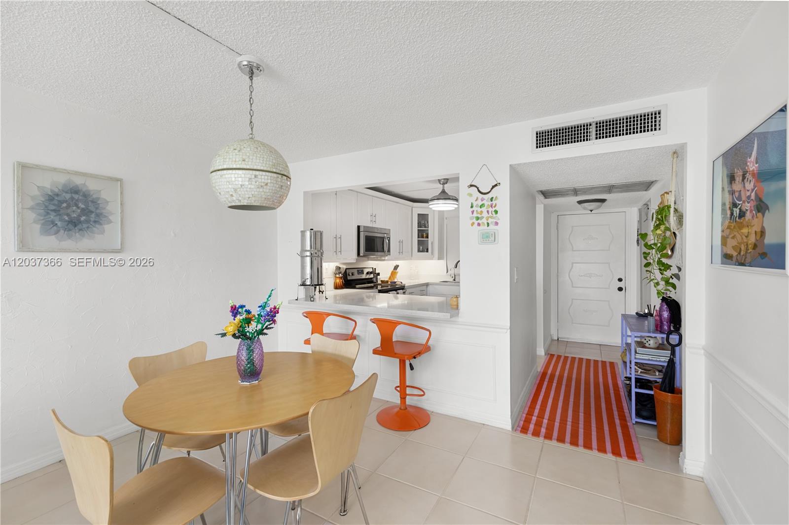 A dining area with a round wooden table sits adjacent to a kitchen pass-through window — 9495 Evergreen Pl # 103, Davie FL 33324, DAVIE, FL