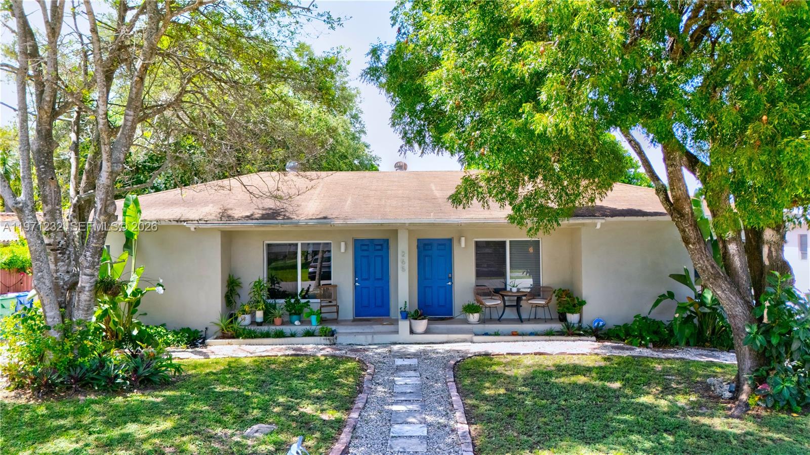 A single-story duplex with two blue front doors, a gravel walkway, and mature trees — 265 NE 116th St, Miami FL 33161, MIAMI, FL
