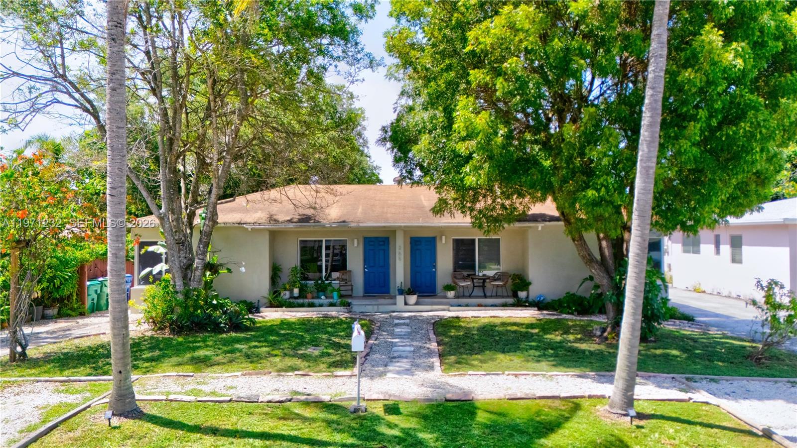 A single-story duplex with two blue front doors, a gravel walkway, and mature trees — 265 NE 116th St, Miami FL 33161, MIAMI, FL