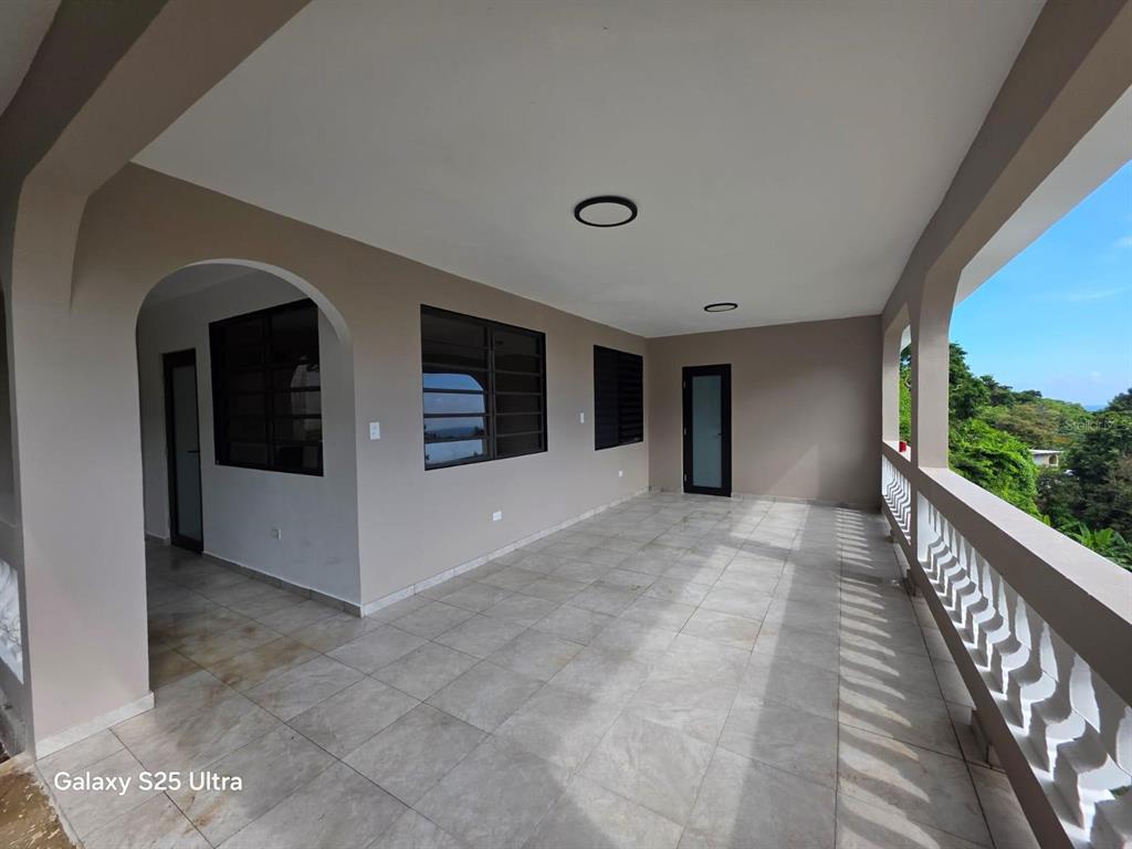 A spacious covered balcony features light-colored tile flooring, beige walls, and a decorative white railing — 290 CALLE CEIBA, PATILLAS, PR