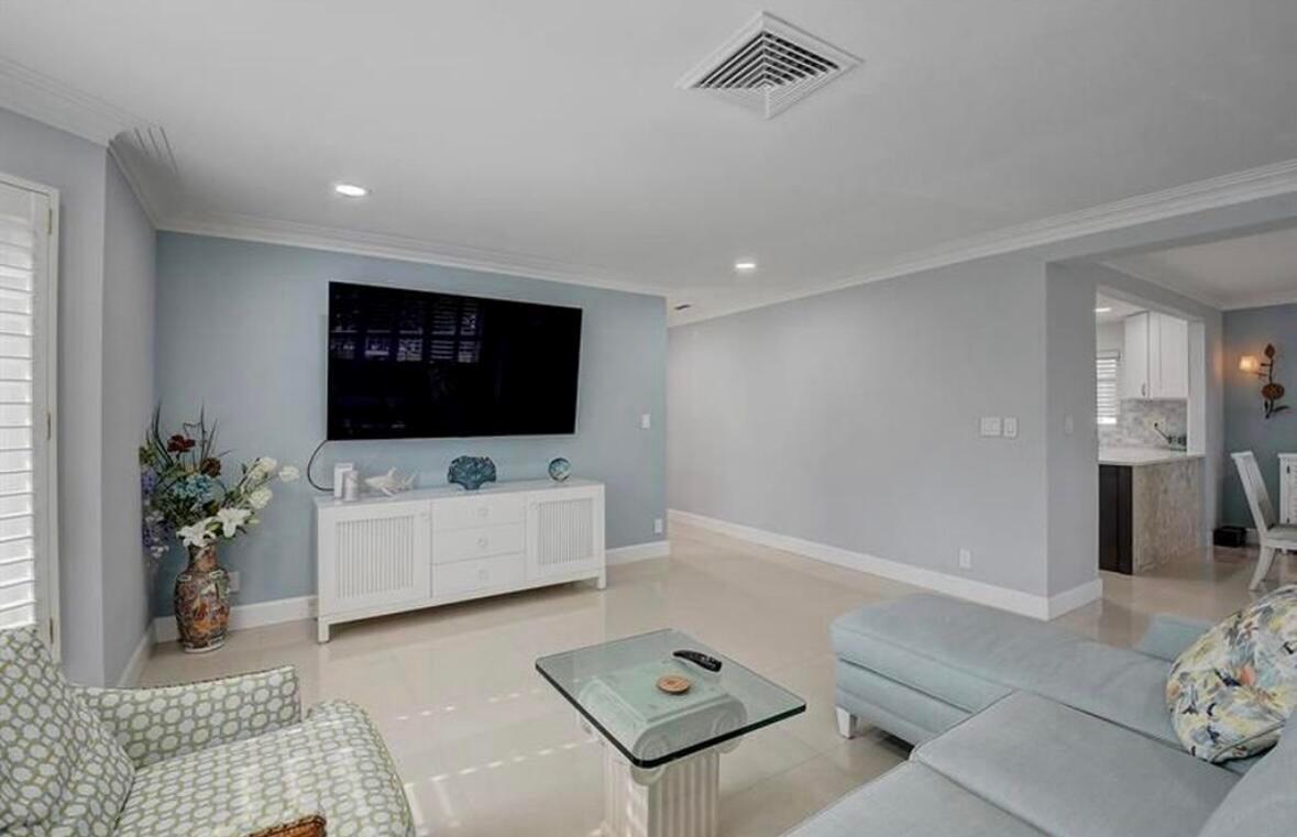 A living room features a wall-mounted television, white media console, and light-colored tile flooring — 1299 S Ocean Boulevard # L5, Boca Raton FL 33432, BOCA RATON, FL