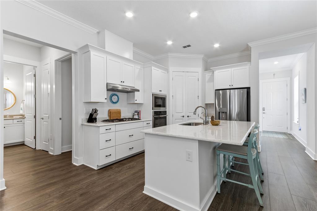 A white kitchen features a central island, stainless steel appliances, and dark wood-look flooring — 95984 Mimosa Drive, FL 32034, FL