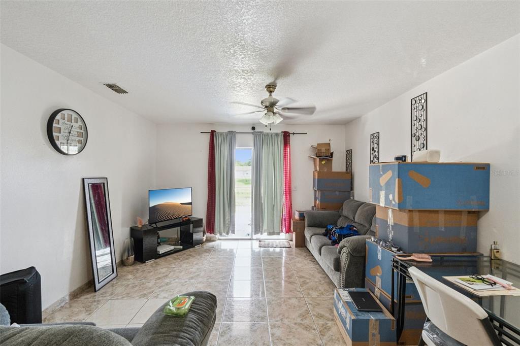 A living room features tile flooring, a ceiling fan, a sliding glass door, and moving boxes — 6833 LONGMEADE LANE, ORLANDO, FL
