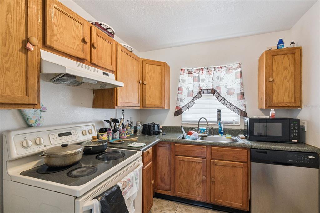 A kitchen features wood cabinets, a white stove, a stainless steel dishwasher, and a window — 6833 LONGMEADE LANE, ORLANDO, FL
