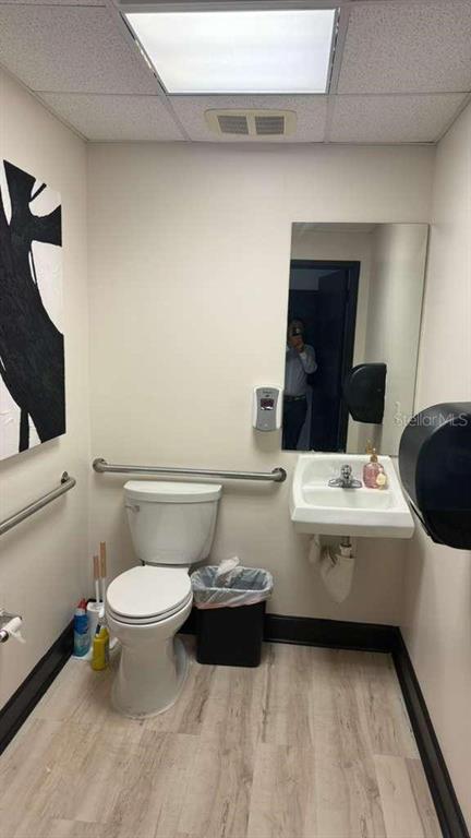 A small, accessible restroom features a white toilet, wall-mounted sink, grab bars, and light flooring — 608 S TAMPANIA AVENUE, TAMPA, FL