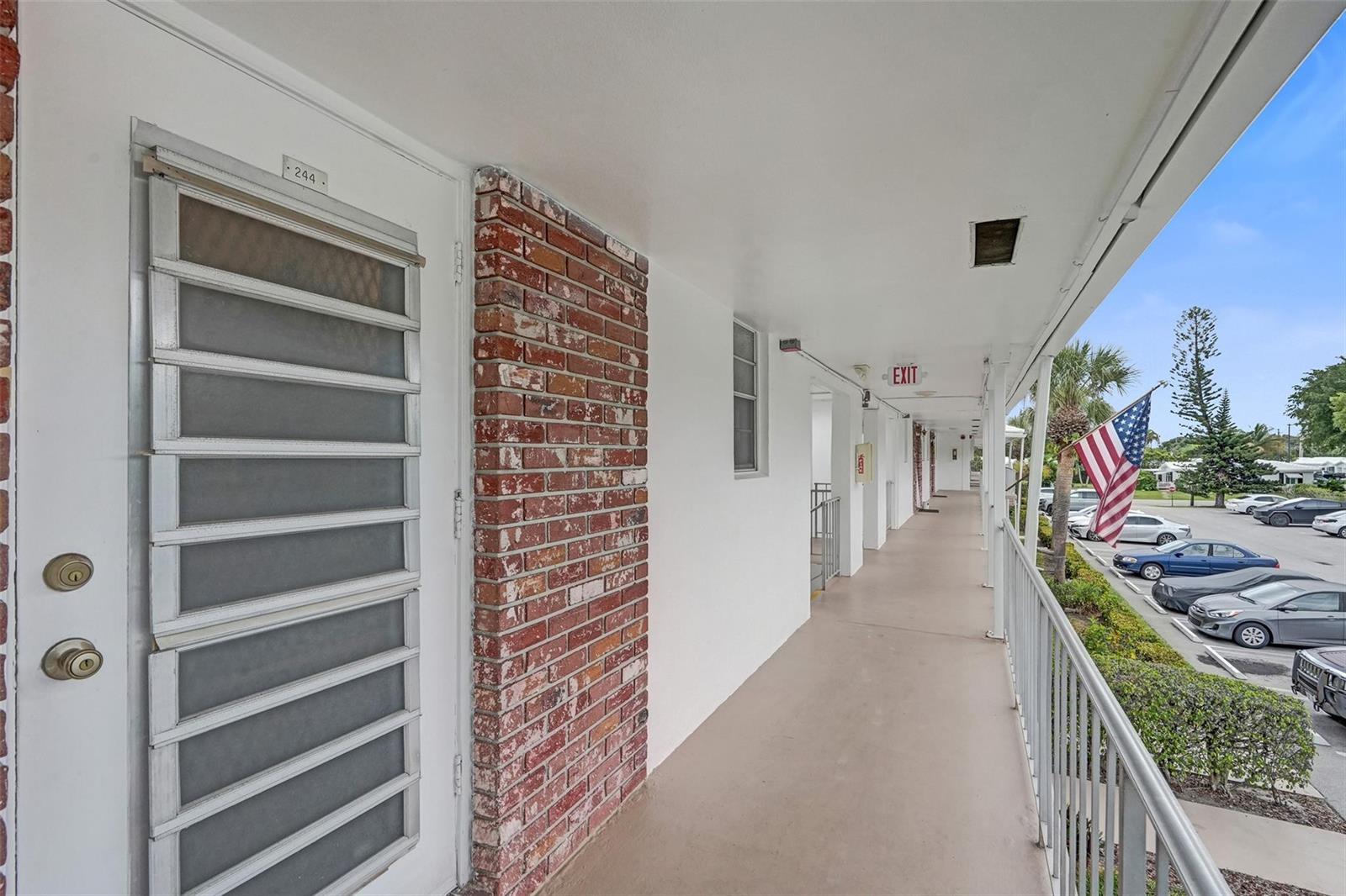 An exterior walkway with a brick accent wall leads to a door numbered 244 — 2475 W Golf Boulevard # 244, Pompano Beach FL 33064, POMPANO BEACH, FL