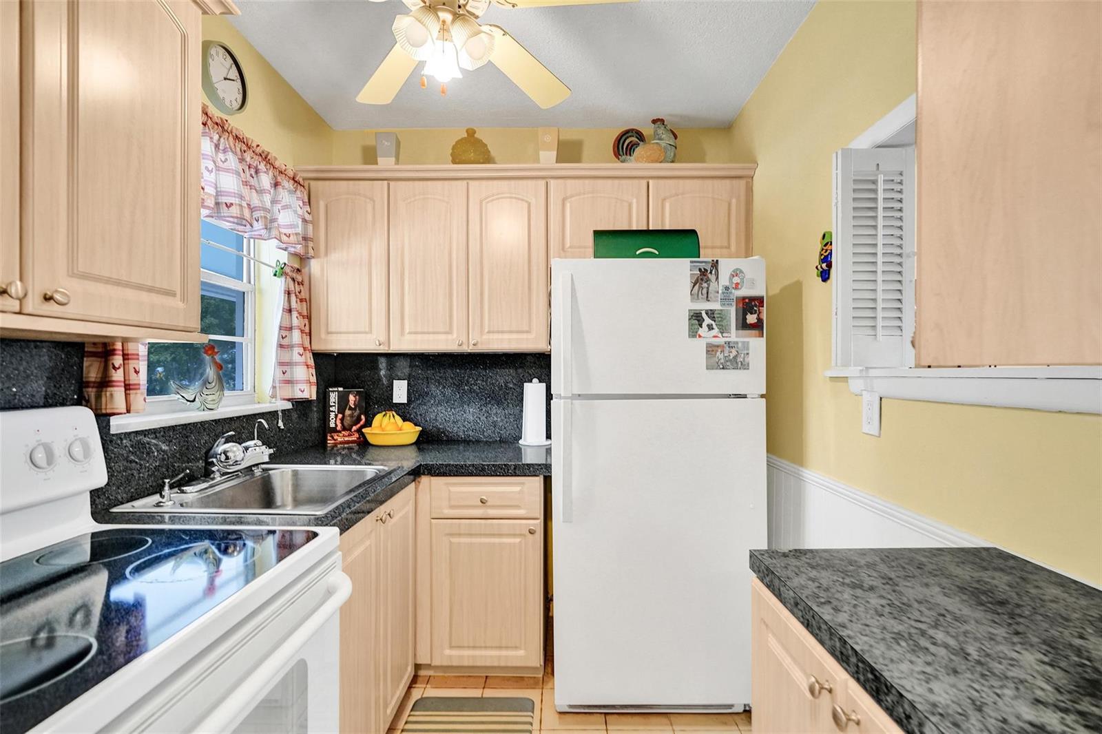 A kitchen features light wood cabinets, dark granite countertops, a white refrigerator, and yellow walls — 2475 W Golf Boulevard # 244, Pompano Beach FL 33064, POMPANO BEACH, FL
