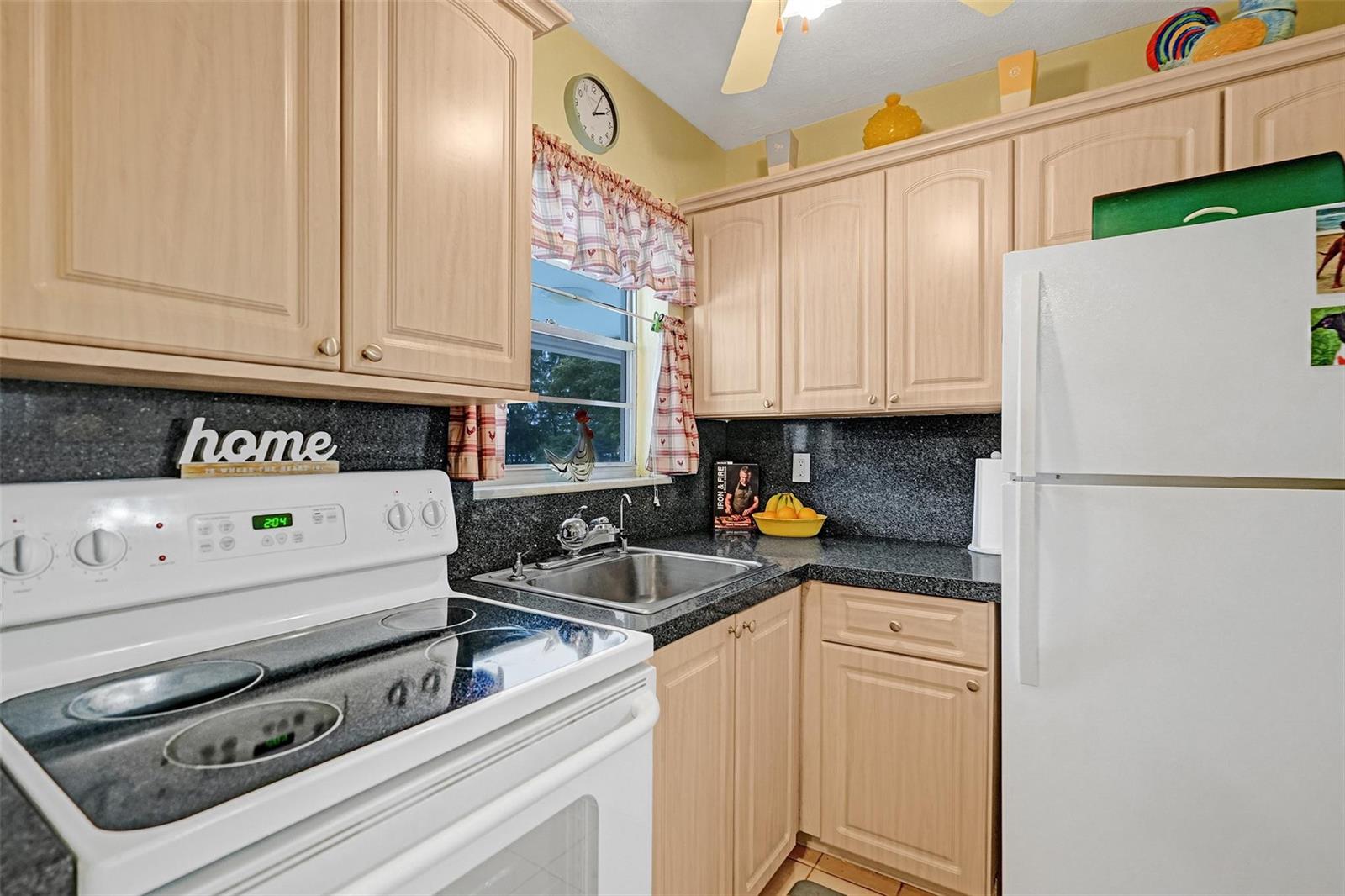A kitchen features light wood cabinets, dark granite countertops, a white stove, and a refrigerator — 2475 W Golf Boulevard # 244, Pompano Beach FL 33064, POMPANO BEACH, FL