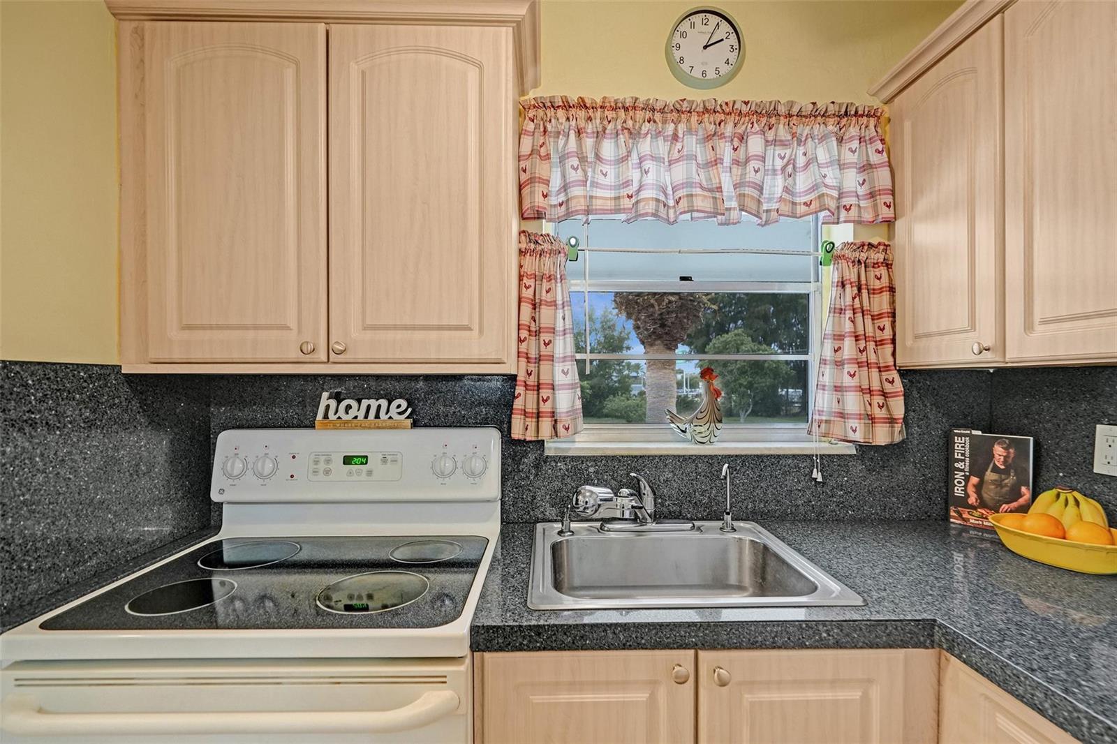 A kitchen features light wood cabinets, dark granite countertops, a stainless steel sink, and a stove — 2475 W Golf Boulevard # 244, Pompano Beach FL 33064, POMPANO BEACH, FL