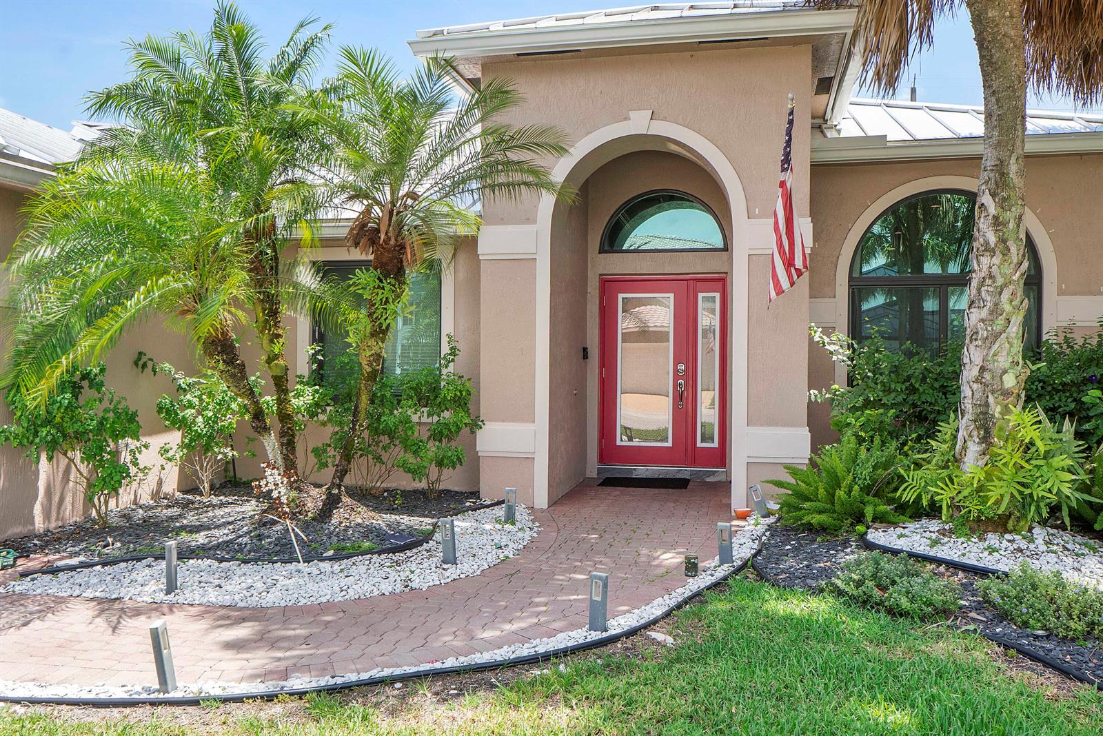 The exterior of a house features a red front door, arched entryway, and palm trees — 12328 Saint Simon Drive, Boca Raton FL 33428, BOCA RATON, FL