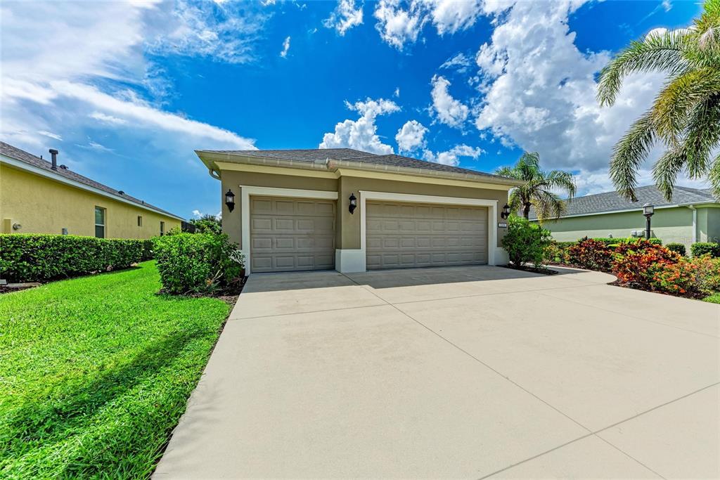 A concrete driveway leads to a two-car garage on a house with tan exterior walls — 12051 FOREST PARK CIRCLE, BRADENTON, FL