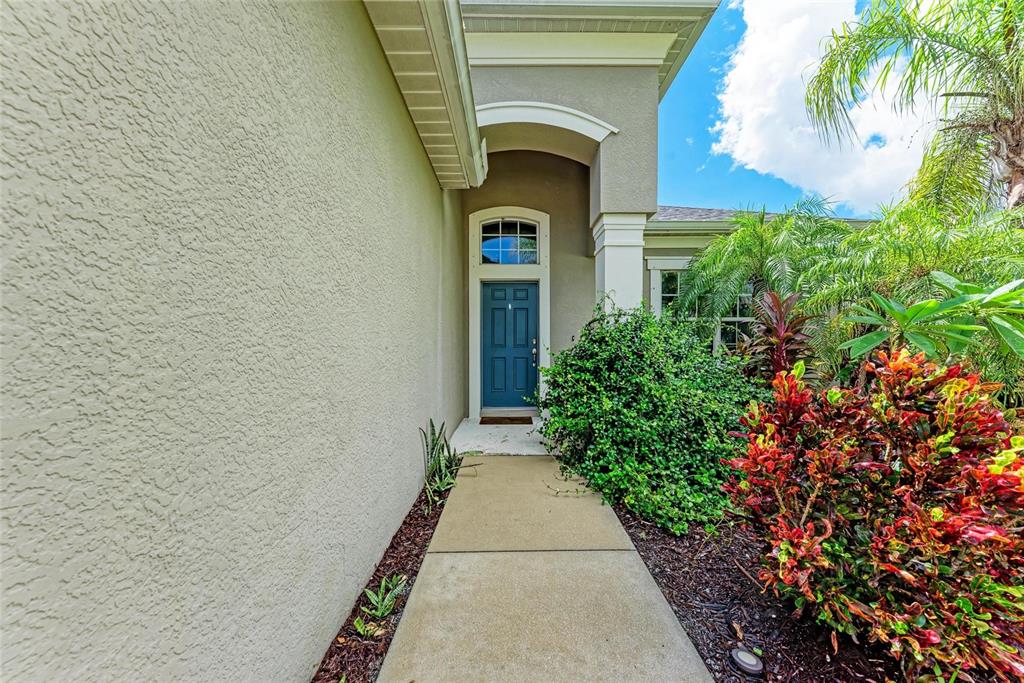 A concrete walkway leads to a blue front door with a transom window under a portico — 12051 FOREST PARK CIRCLE, BRADENTON, FL