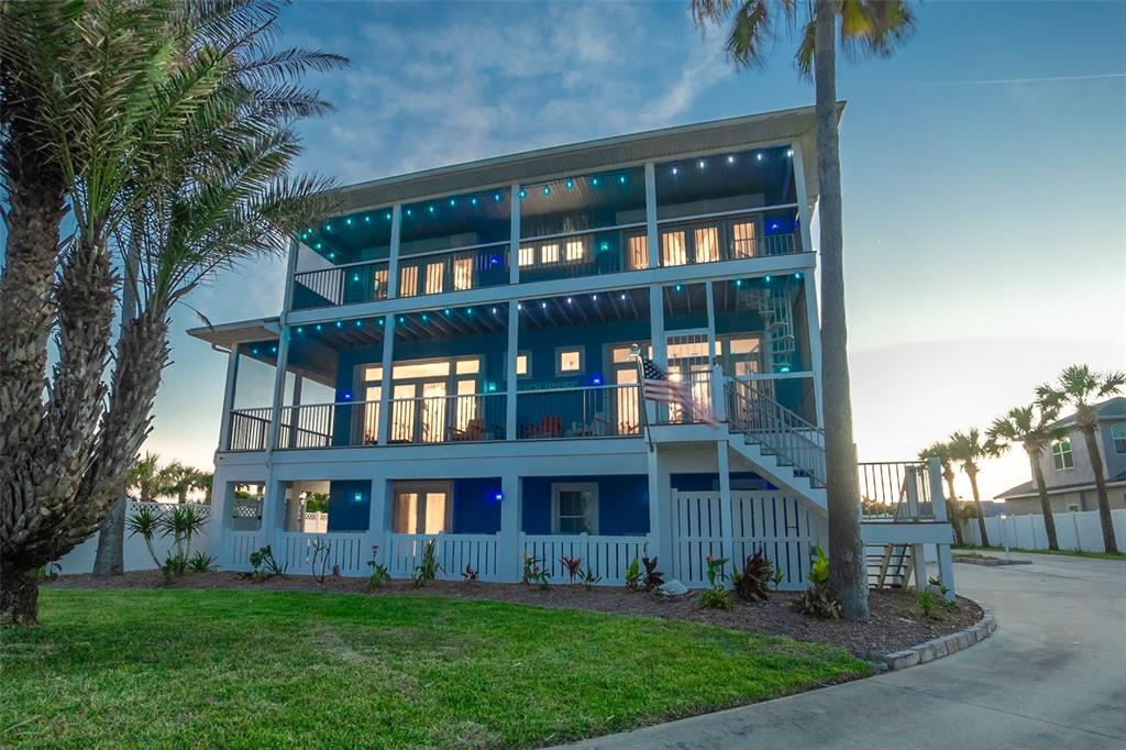 A three-story blue beach house with wrap-around porches and exterior lighting at dusk — 1807 N CENTRAL AVENUE, FLAGLER BEACH, FL