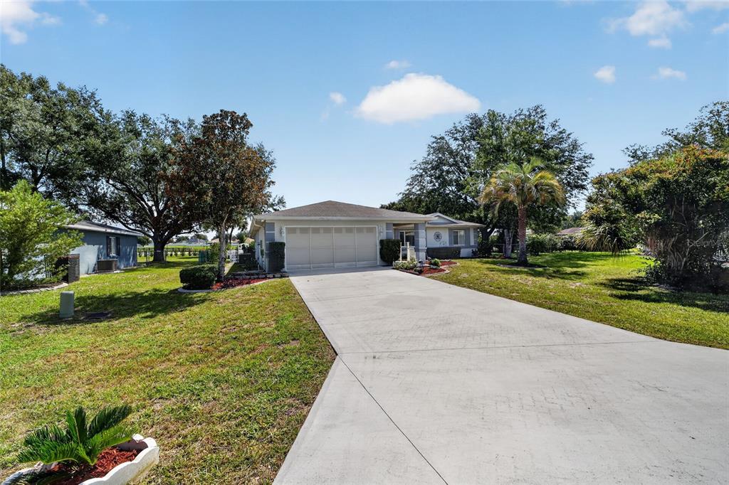 A single-story house with a large concrete driveway, a two-car garage, and surrounding trees — 10036 SW 62ND CIRCLE, OCALA, FL