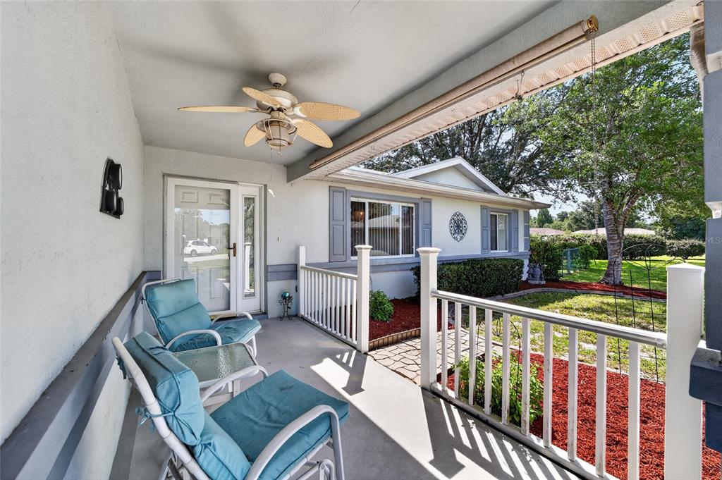 A covered porch features two blue chairs, a ceiling fan, and a white railing — 10036 SW 62ND CIRCLE, OCALA, FL
