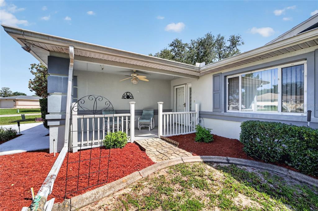 A covered front porch with a white railing, ceiling fan, and stone walkway entrance — 10036 SW 62ND CIRCLE, OCALA, FL