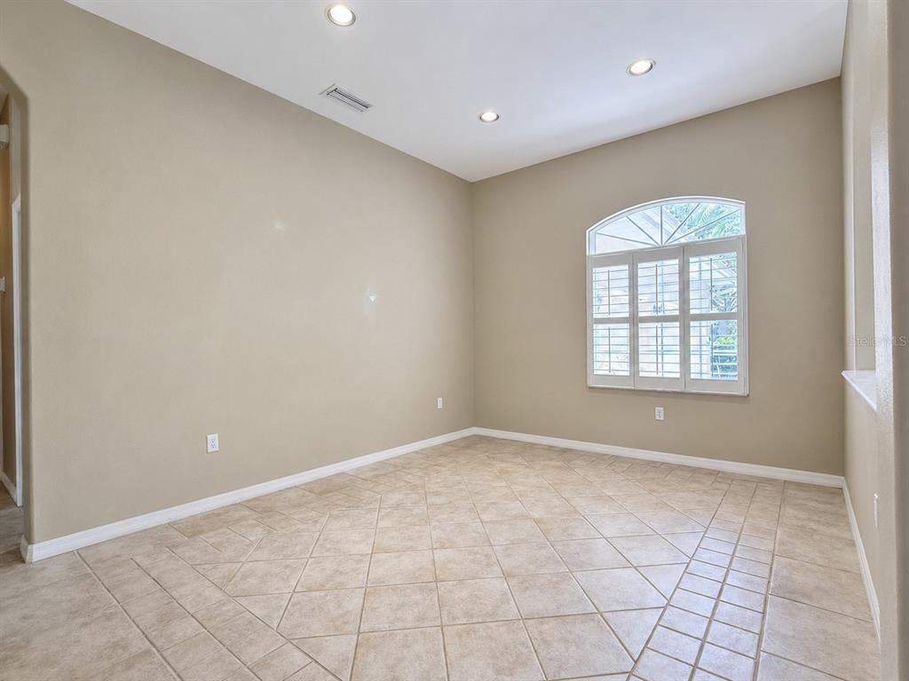 An empty room with beige walls, tile flooring, recessed lighting, and a window with shutters — 4625 SWEETMEADOW CIRCLE, SARASOTA, FL