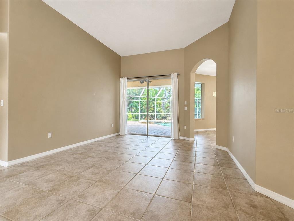 An empty room with beige walls, tile flooring, and sliding glass doors leading to a pool — 4625 SWEETMEADOW CIRCLE, SARASOTA, FL