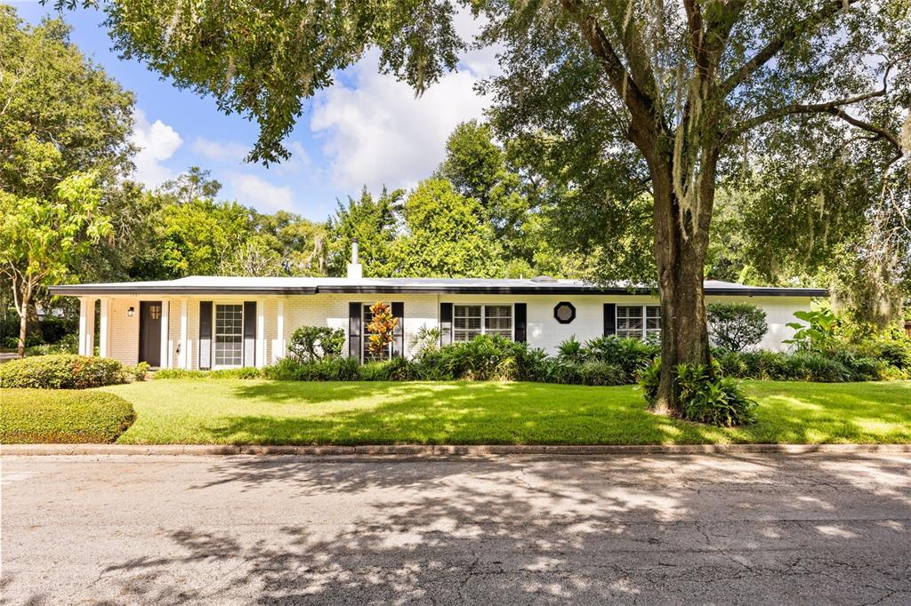 A single-story white brick house with black shutters sits behind a manicured lawn and trees — 1981 BLUE RIDGE ROAD, WINTER PARK, FL