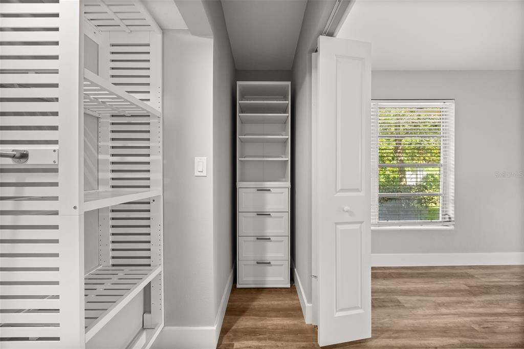 A closet with white shelving and drawers sits next to a room with wood flooring — 1981 BLUE RIDGE ROAD, WINTER PARK, FL
