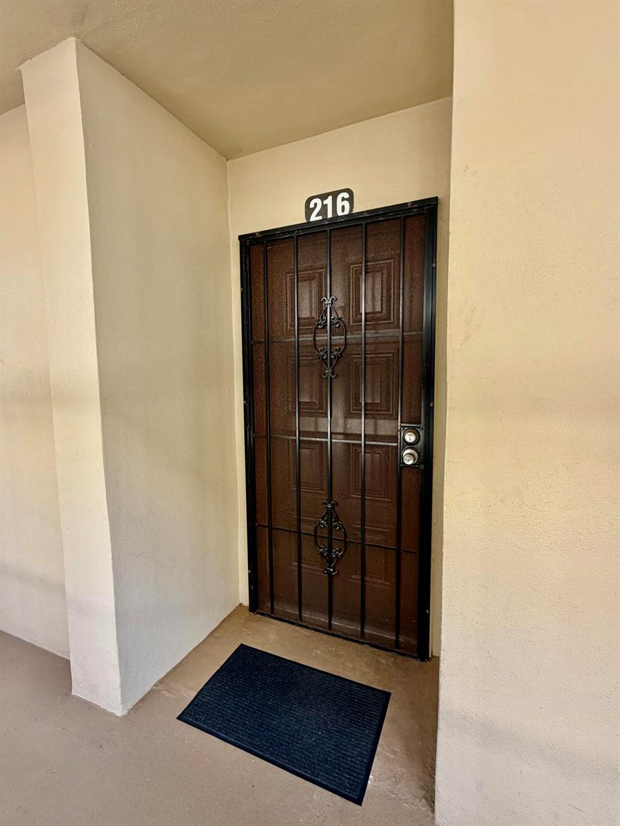 A brown front door with a black security gate is labeled with the number 216 — 5280 Las Verdes Circle # 216, Delray Beach FL 33484, DELRAY BEACH, FL