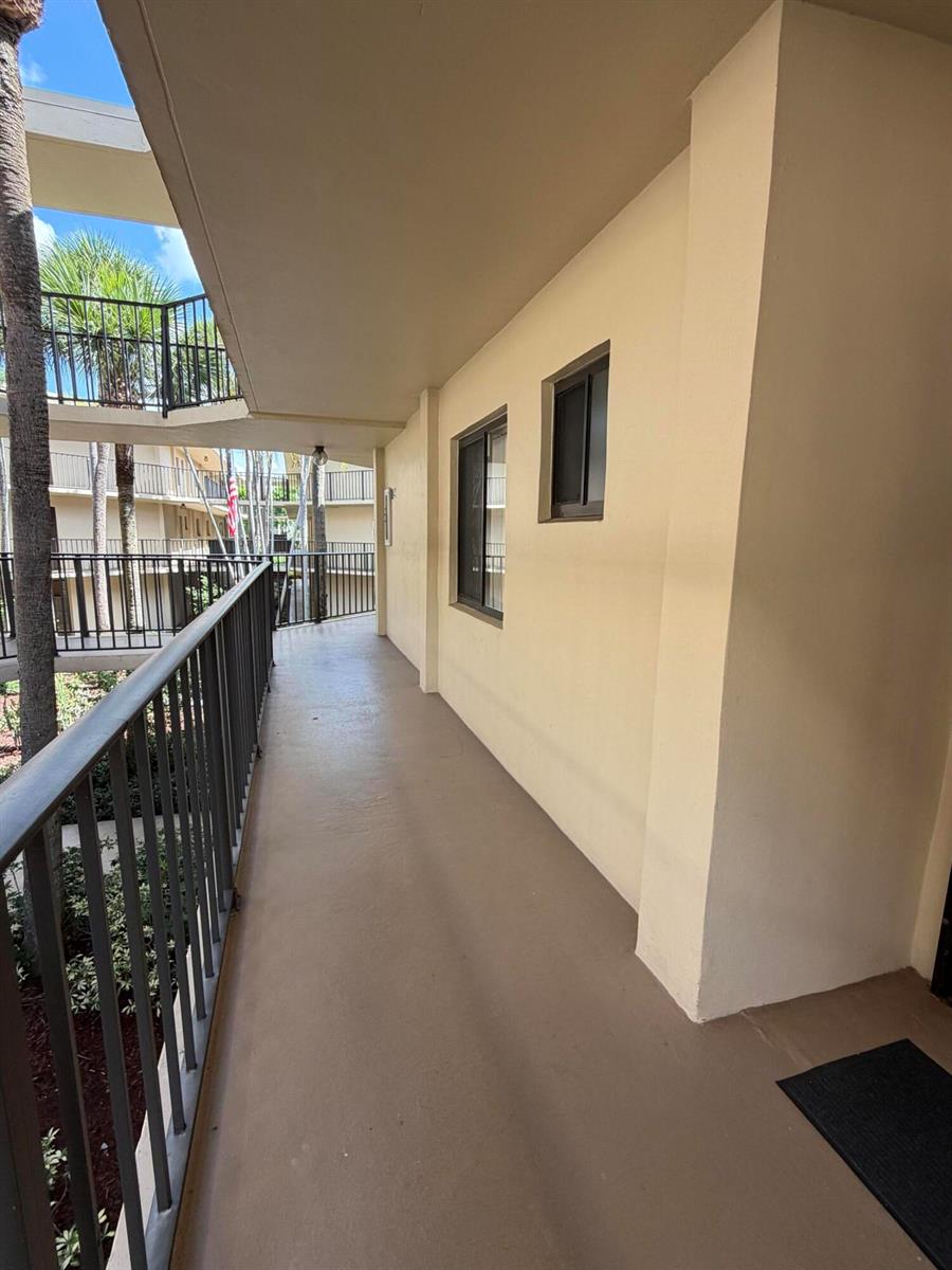An outdoor walkway with a metal railing overlooks a courtyard with palm trees — 5280 Las Verdes Circle # 216, Delray Beach FL 33484, DELRAY BEACH, FL