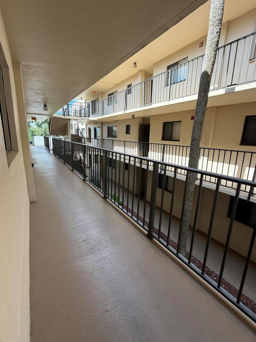 An outdoor apartment building walkway with metal railings and a palm tree — 5280 Las Verdes Circle # 216, Delray Beach FL 33484, DELRAY BEACH, FL