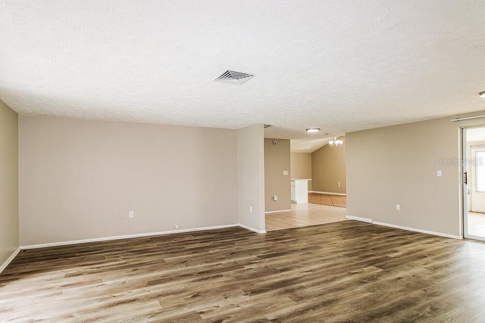 An empty living room features light beige walls, wood-look flooring, and a ceiling vent — 7043 FIRESIDE DRIVE, PORT RICHEY, FL