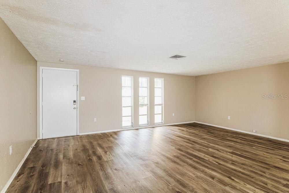 An empty room with beige walls, wood-look flooring, and three vertical windows — 7043 FIRESIDE DRIVE, PORT RICHEY, FL