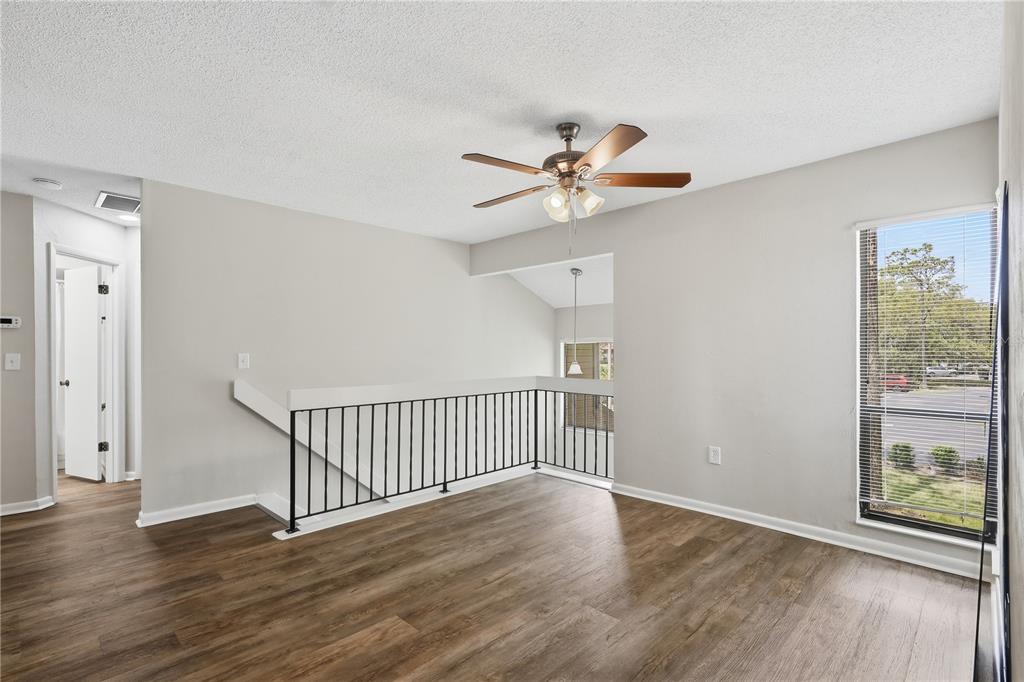 An empty room with wood-look flooring, a ceiling fan, and a black metal stair railing — 16 HEMBURY LANE UNIT 16, PALM COAST, FL