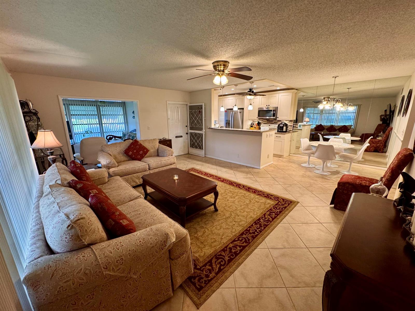 A living room with tile floors, a patterned sofa, and an open kitchen with white cabinets — 1252 Club Drive W # D, Delray Beach FL 33445, DELRAY BEACH, FL