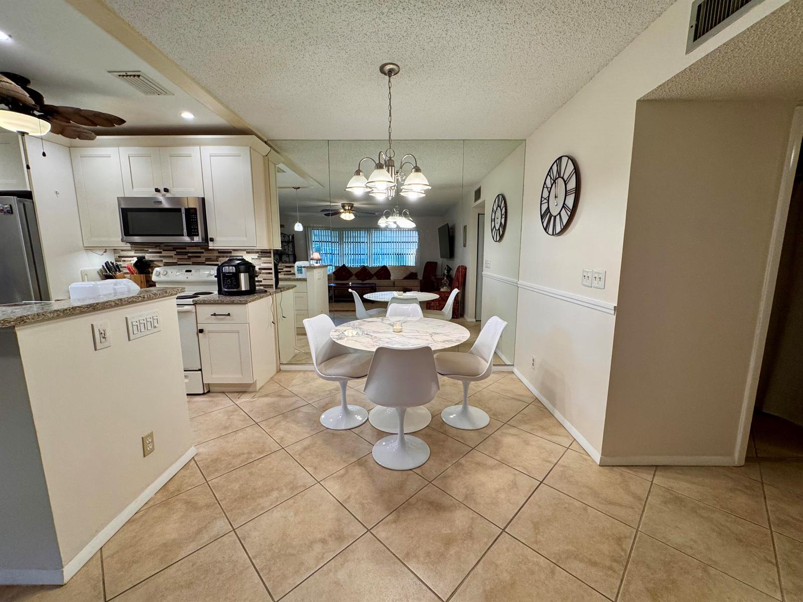 A kitchen with white cabinets and a dining area featuring a round table and mirrors — 1252 Club Drive W # D, Delray Beach FL 33445, DELRAY BEACH, FL