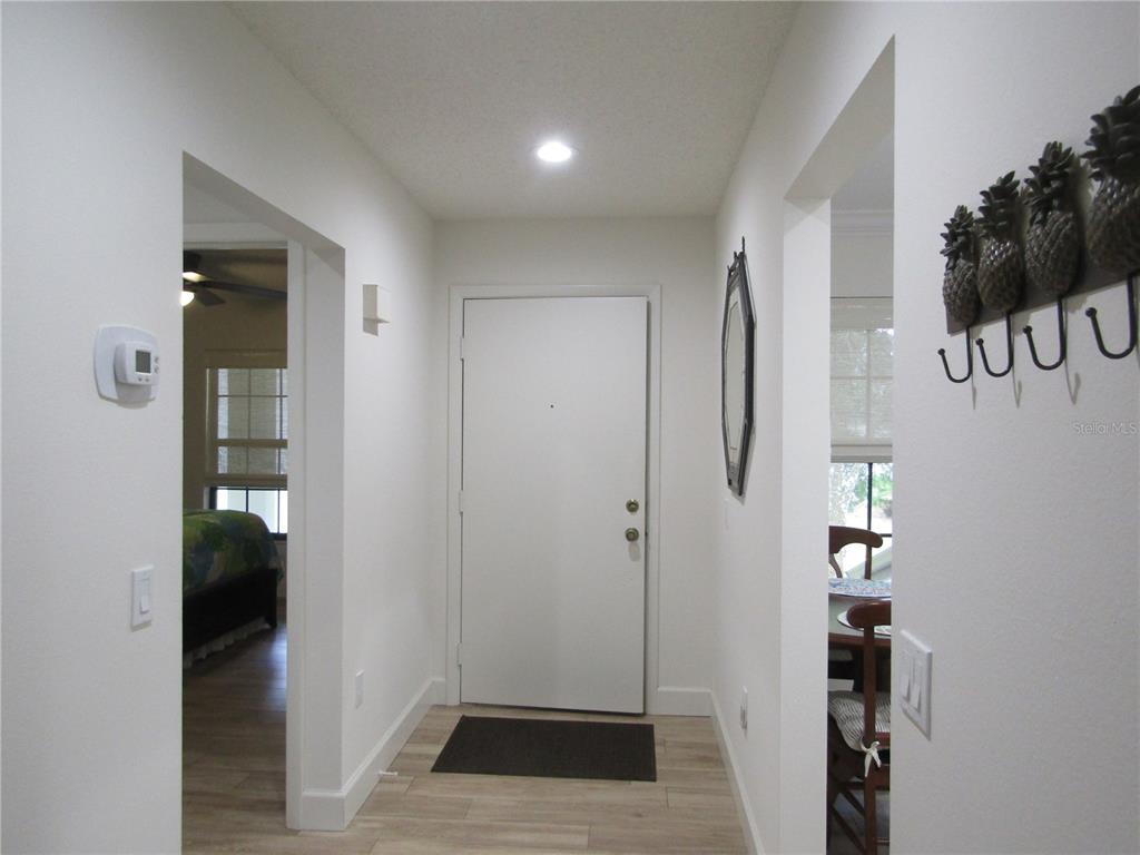 A white front door sits at the end of a hallway with light wood flooring — 4757 WINSLOW BEACON UNIT 20, SARASOTA, FL