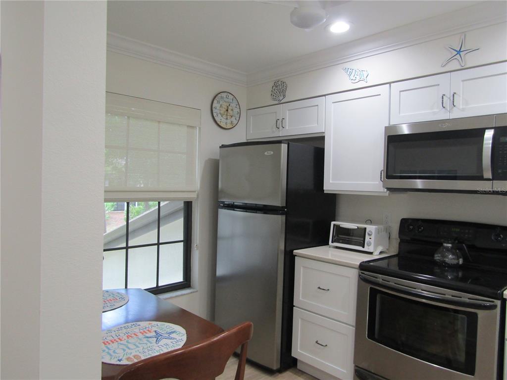 A kitchen features stainless steel appliances, white cabinets, and a small dining table by a window — 4757 WINSLOW BEACON UNIT 20, SARASOTA, FL