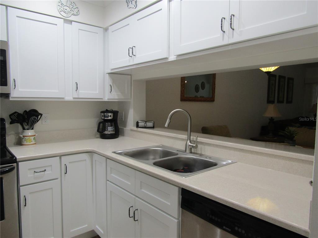 A kitchen with white cabinets, light countertops, a double sink, and a pass-through window — 4757 WINSLOW BEACON UNIT 20, SARASOTA, FL