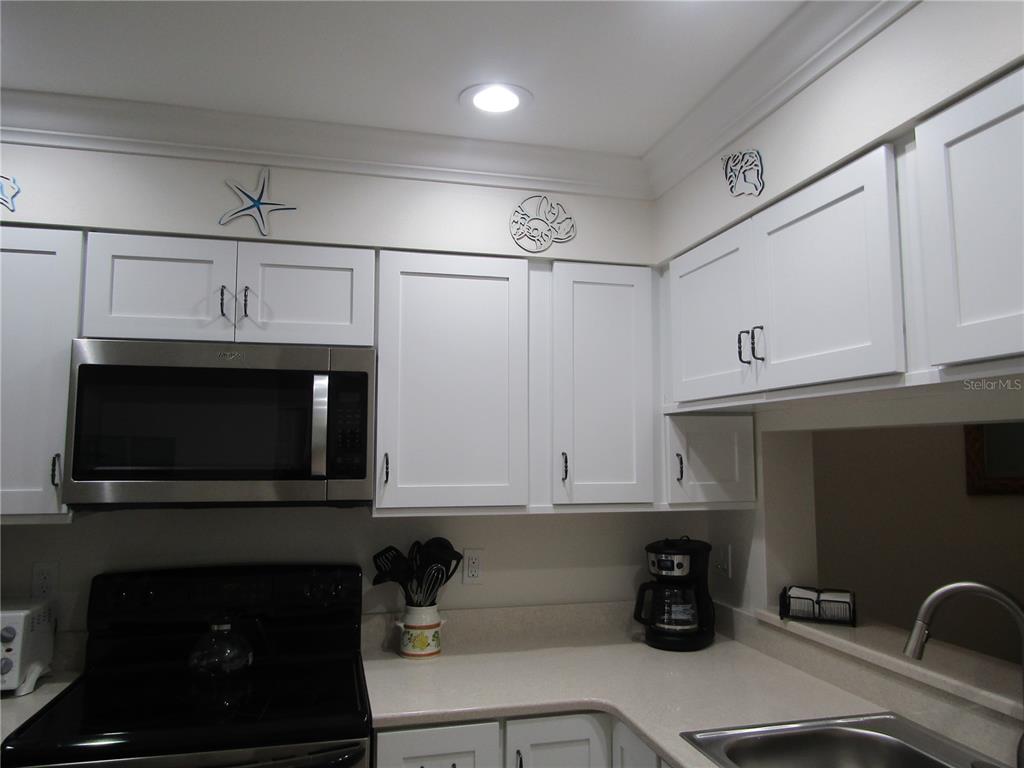 A kitchen features white cabinets, stainless steel appliances, and decorative wall art above the cabinets — 4757 WINSLOW BEACON UNIT 20, SARASOTA, FL