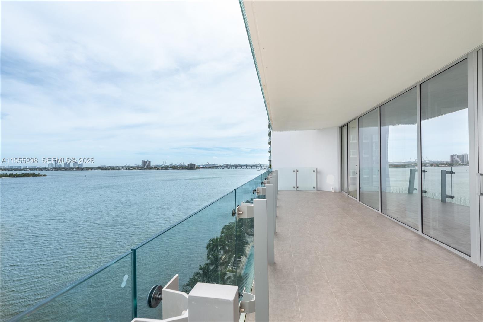 A spacious balcony with glass railings overlooks a large body of water — 700 NE 26th Ter # 903, Miami FL 33137, MIAMI, FL