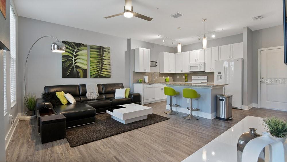 An open-concept living room and kitchen feature a black leather sectional, island, and white cabinetry — 1861 HOUSTON STREET, KISSIMMEE, FL