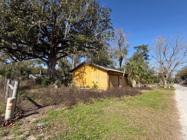 A yellow wooden shed stands in a grassy yard beneath a large tree — 1219 N PARIS STREET, BELL, FL