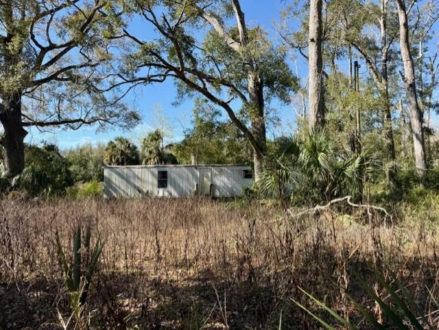 A single-wide mobile home sits in a field surrounded by trees and tall, dry grass — 1219 N PARIS STREET, BELL, FL
