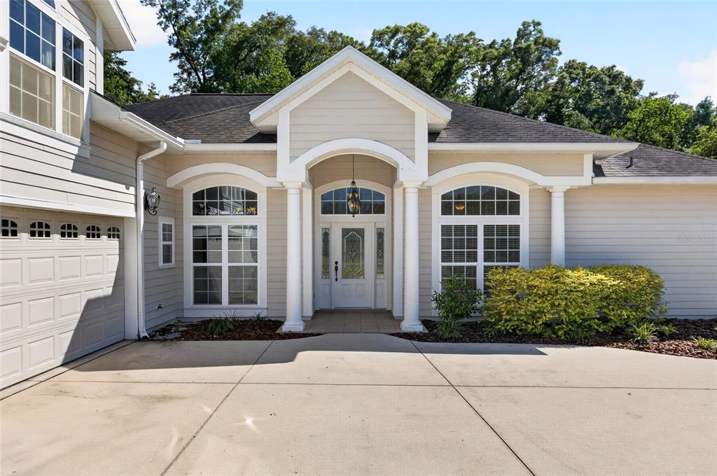 A beige house exterior features a covered entryway with white columns and a concrete driveway — 26807 SW 20TH PLACE, NEWBERRY, FL