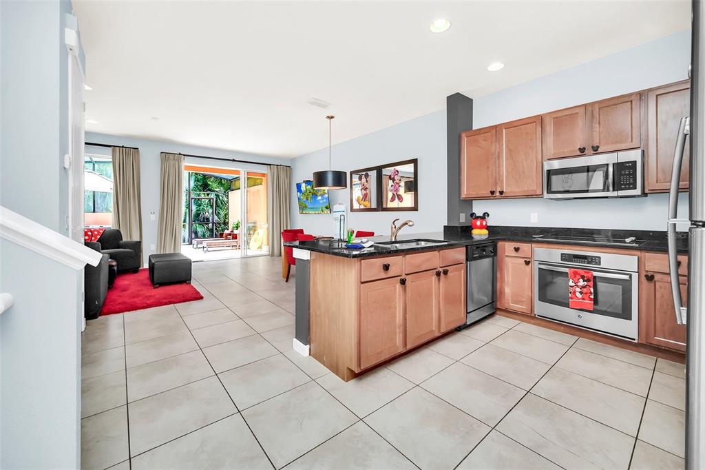 A kitchen with light wood cabinets and a dark island opens into a living area — 2607 CORVETTE LANE, KISSIMMEE, FL
