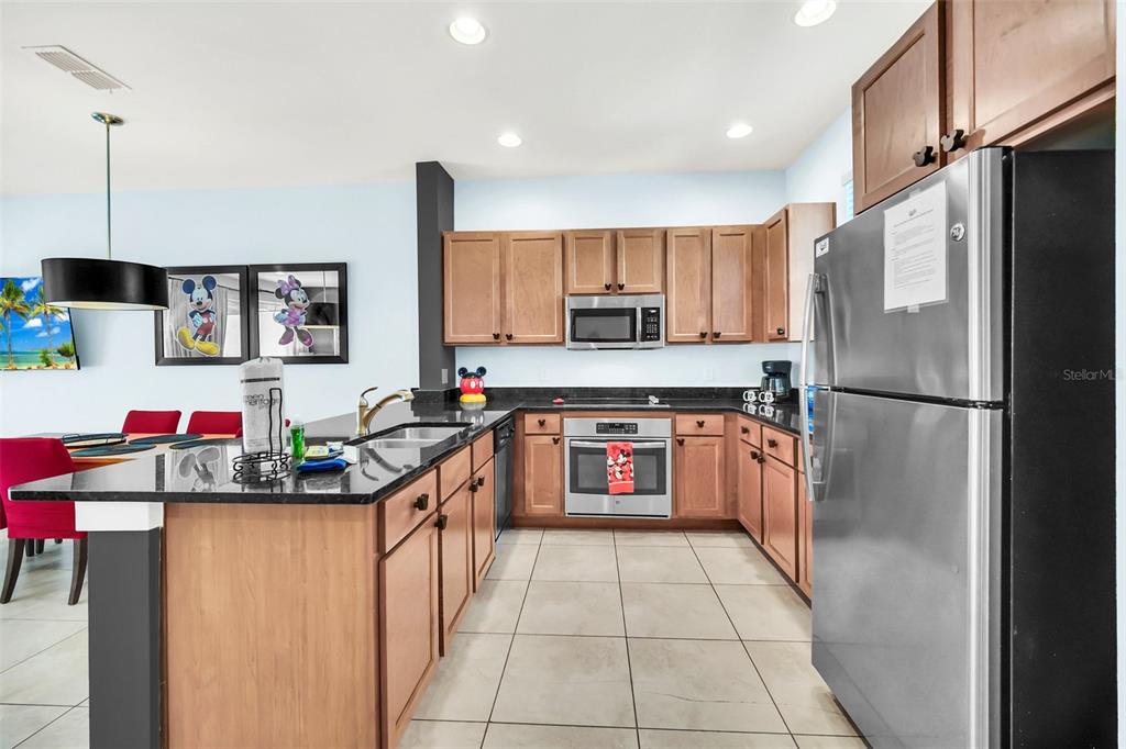 A kitchen features wood cabinets, stainless steel appliances, and a black granite island countertop — 2607 CORVETTE LANE, KISSIMMEE, FL