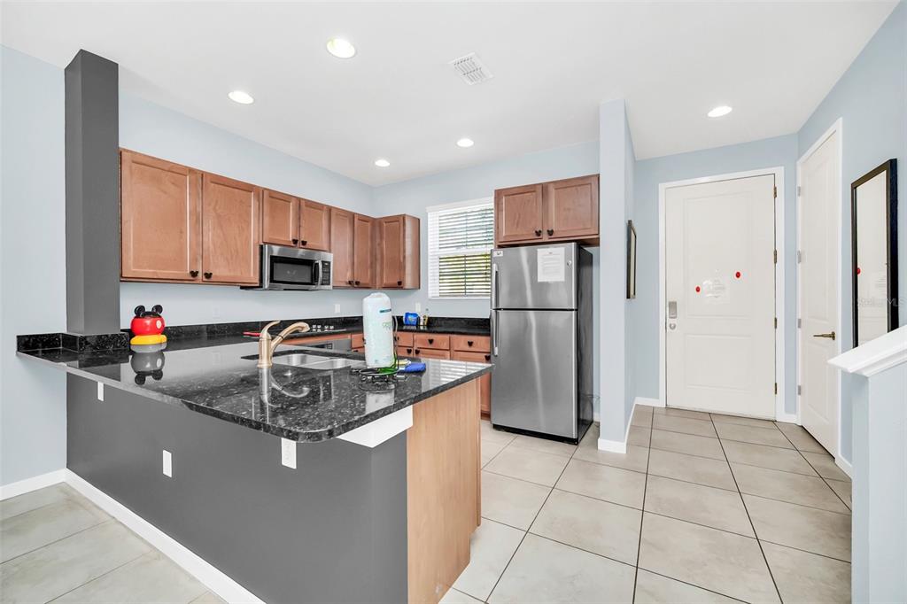 A kitchen features wood cabinets, dark granite countertops, stainless steel appliances, and light tile flooring — 2607 CORVETTE LANE, KISSIMMEE, FL