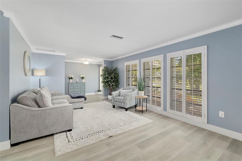 A living room with light blue walls, gray flooring, a sectional sofa, and plantation shutters — 3304 SPRING MILL CIRCLE, SARASOTA, FL