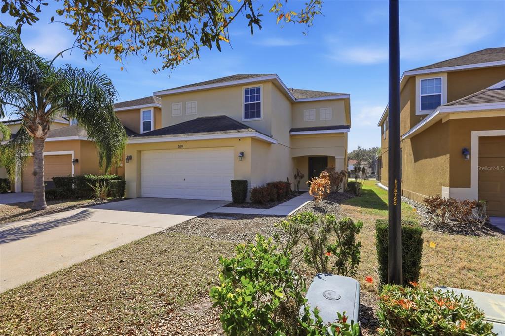 A two-story suburban house with a beige exterior, a two-car garage, and a palm tree — 2620 SANTOSH COVE, KISSIMMEE, FL